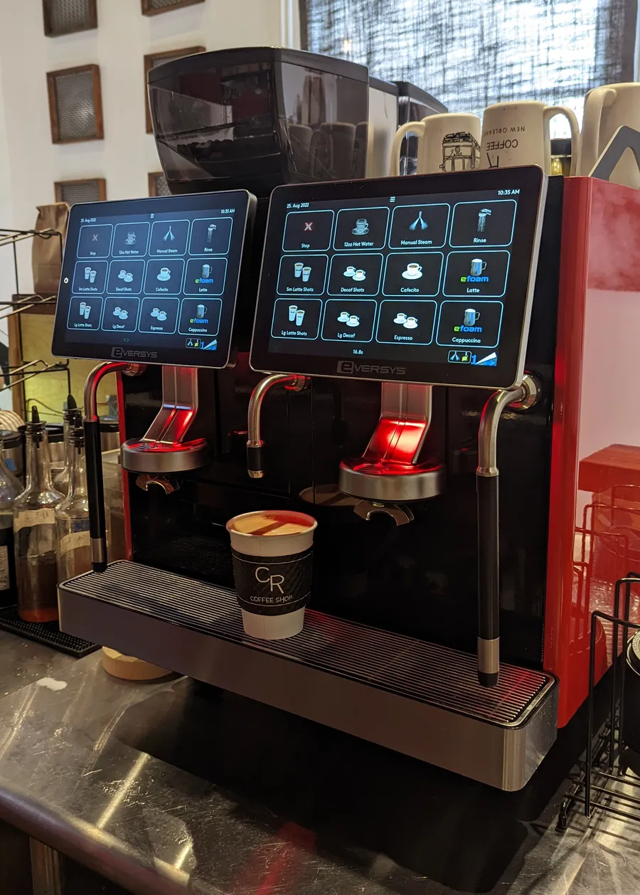 A red and black two-group Eversys espresso machine on the counter at CR Coffee Shop, with a CR branded cup under the spouts