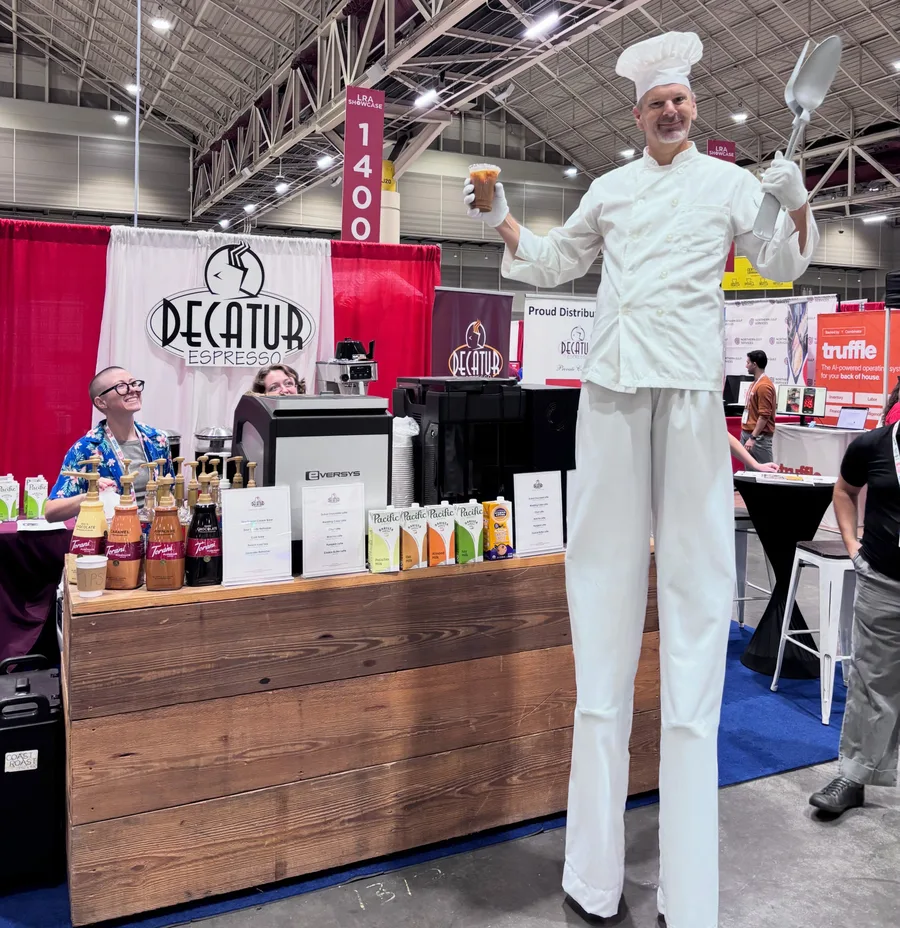 The Decatur Espresso booth at the Louisiana Restaurant Association Showcase, with staff pouring drinks and a chef on stilts holding an iced coffee