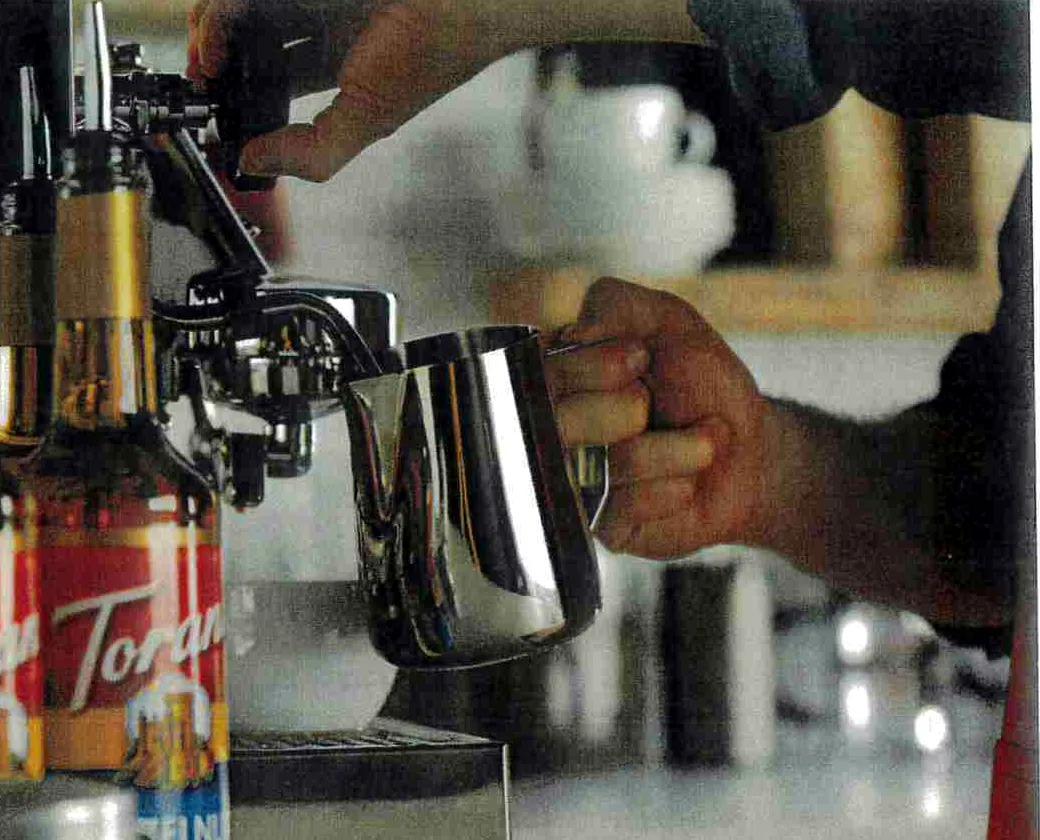 Steaming milk on an espresso machine beside a rack of Torani syrups